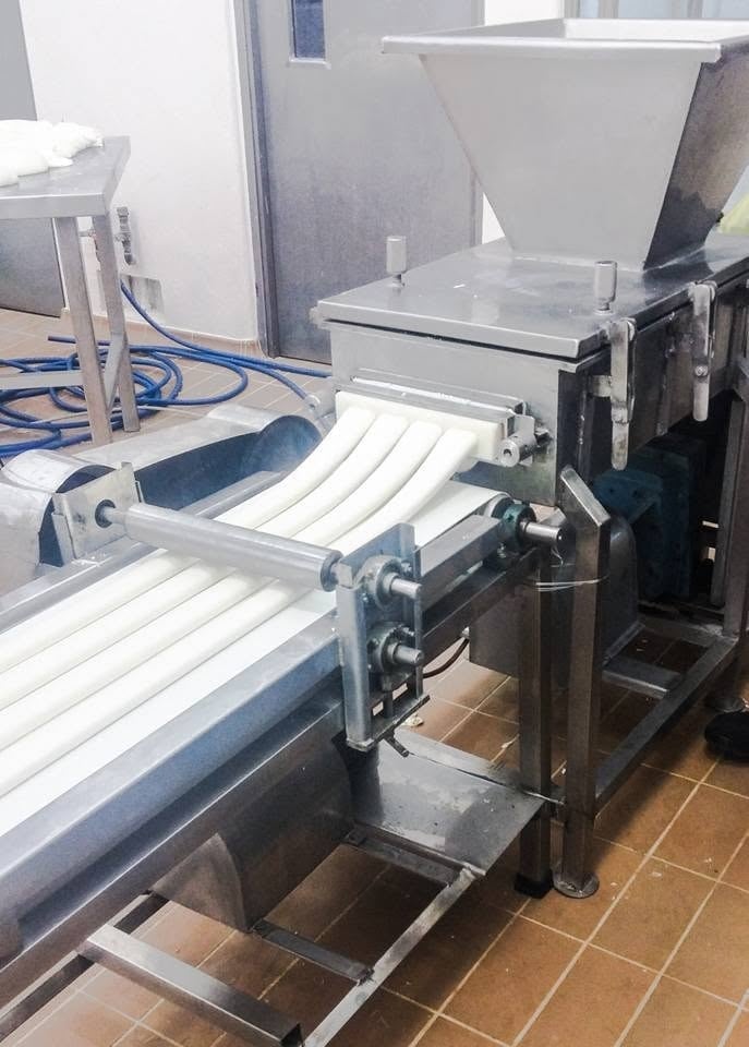 Extrusor KIN-ROD en operación mostrando la boquilla de extrusión intercambiable formando tiras de queso sobre banda transportadora en planta alimentaria