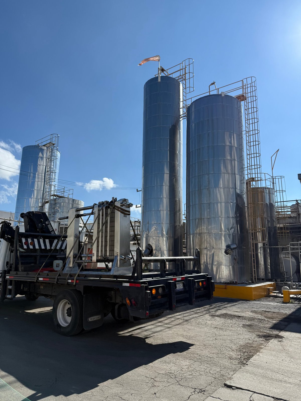 Silos e intercambiadores de calor de acero inoxidable en planta industrial con plataforma y grúa en piso de concreto