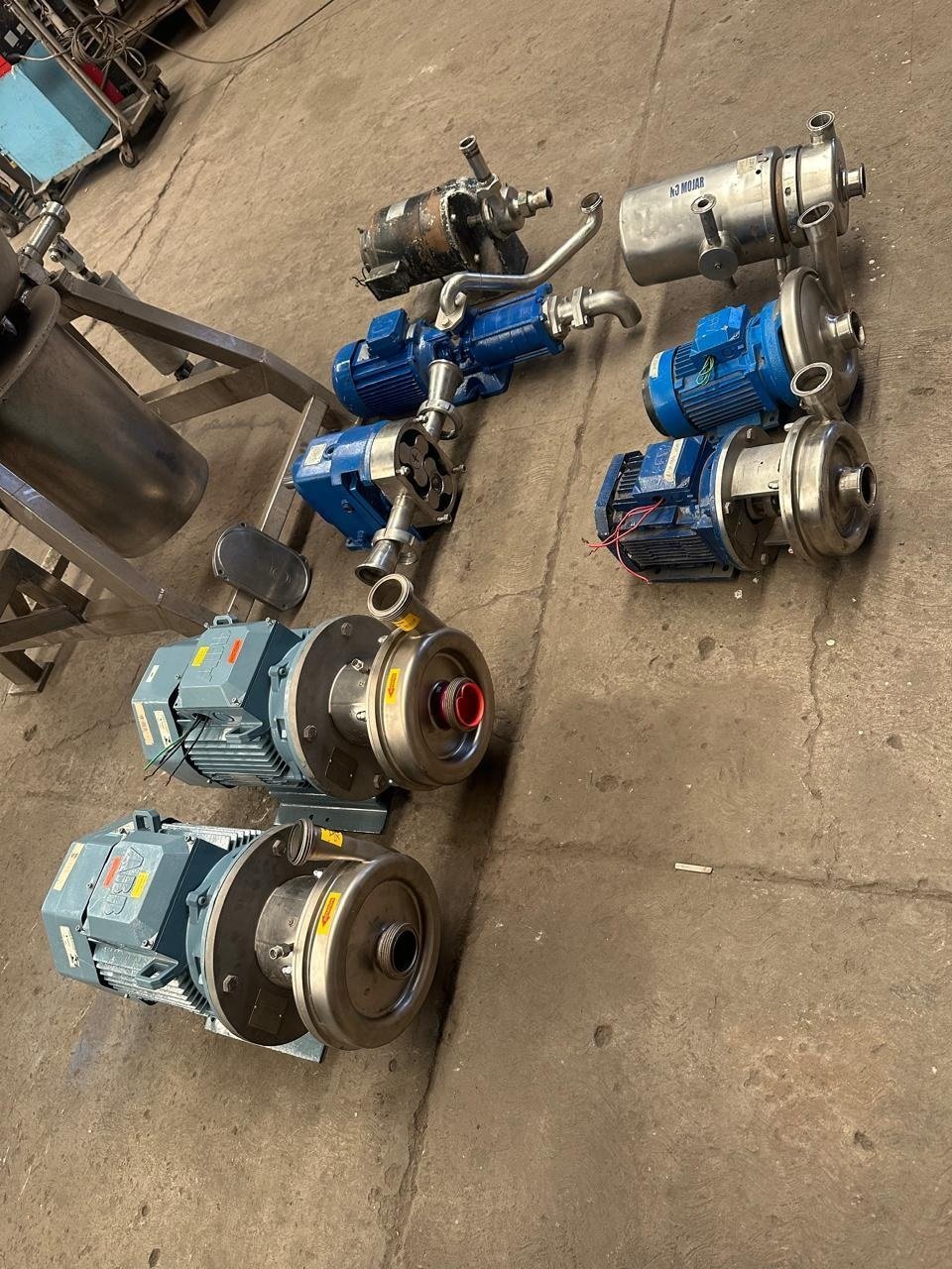 Bombas sanitarias de acero inoxidable reacondicionadas con motor eléctrico azul, dispuestas en piso de taller