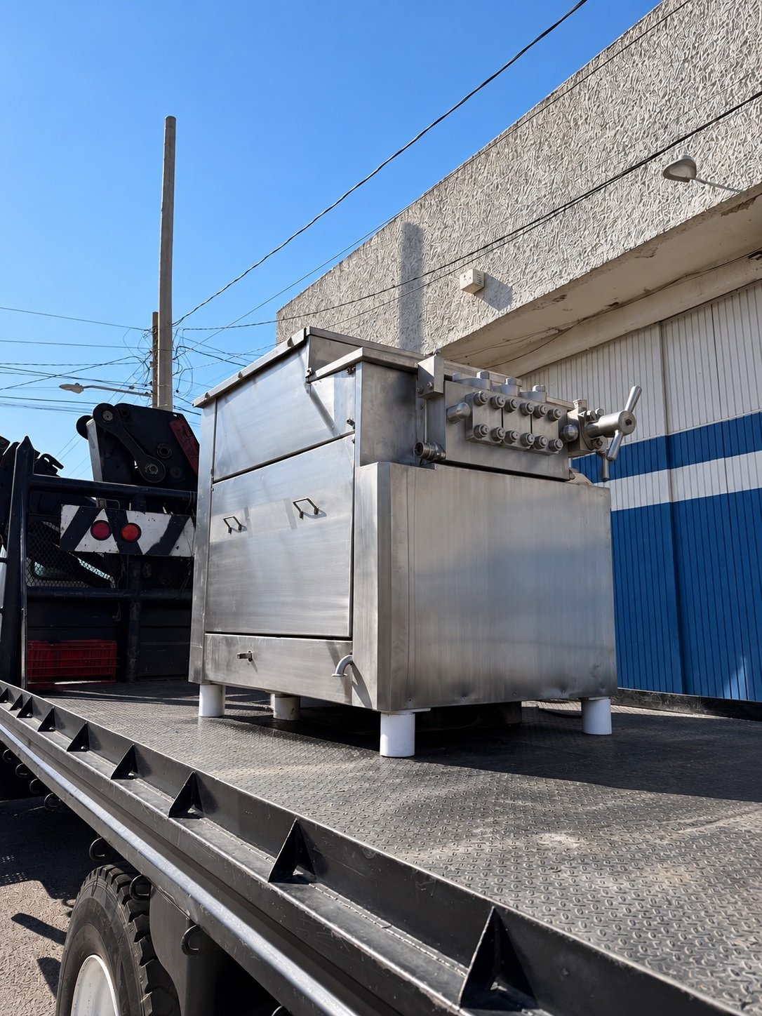 Homogenizador de acero inoxidable reacondicionado por KIN-ROD sobre plataforma de camión de carga, listo para entrega, con conexiones de proceso visibles