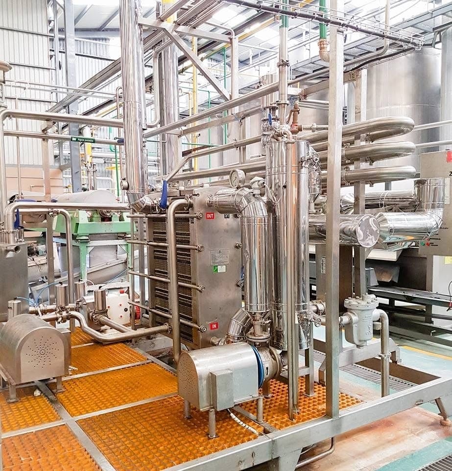 Línea de pasteurización KIN-ROD instalada en planta láctea con intercambiador de placas, tuberías, bomba de alimentación y tablero de control sobre piso industrial naranja